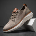 Khaki mesh sneaker with brown leather trim and white cushioned sole propped diagonally against a white geometric block