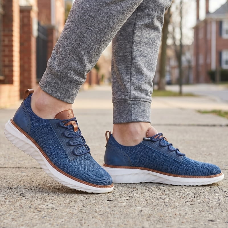 Person wearing navy blue mesh sneakers with brown trim and gray joggers, walking on a residential sidewalk