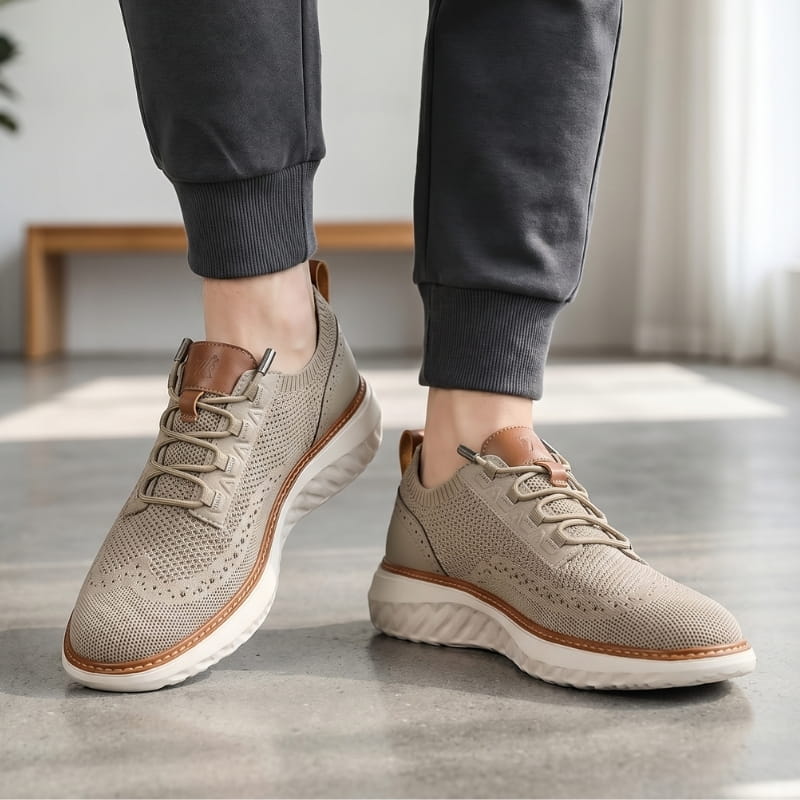 Person wearing khaki mesh sneakers with brown trim and dark gray joggers, standing on a concrete floor indoors