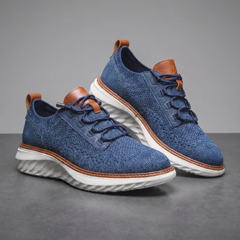 Pair of navy blue mesh sneakers with brown trim and white soles stacked at an angle on a gray studio background