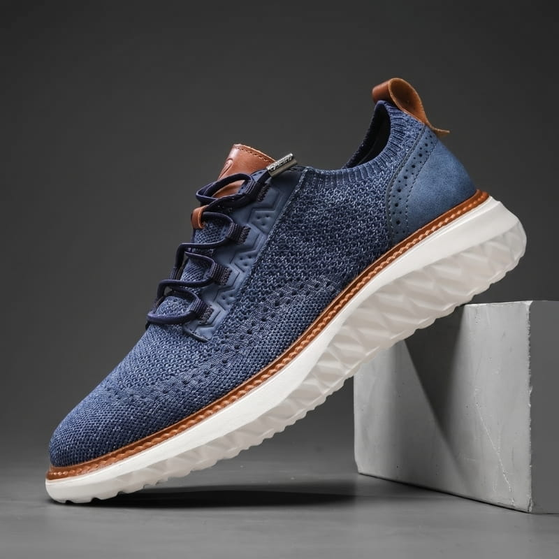 Navy blue mesh sneaker with brown leather trim and white cushioned sole propped diagonally against a concrete block