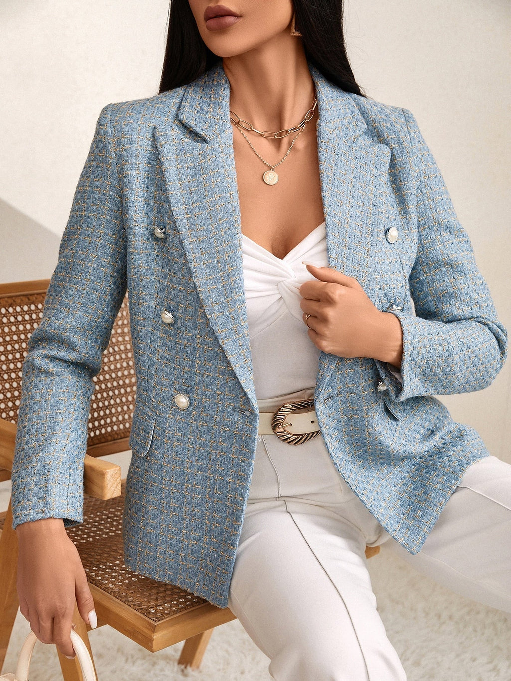Woman wearing a light blue tweed blazer with gold-tone buttons and tailored fit over a white top and light trousers.