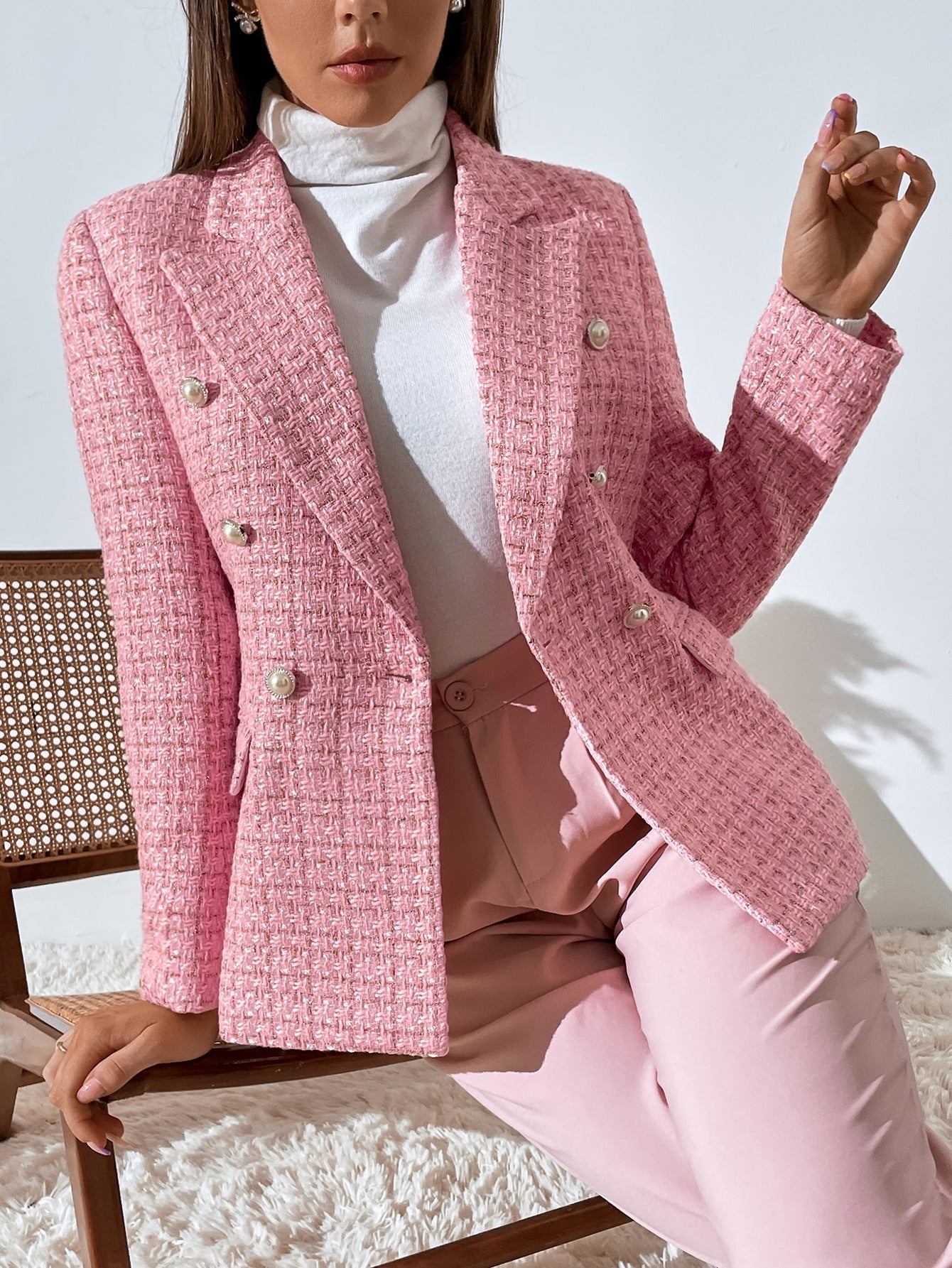 Woman wearing a pink textured tweed blazer with gold-tone buttons, notched lapels, flap pockets, and tailored fit, paired with pink trousers and a white turtleneck.