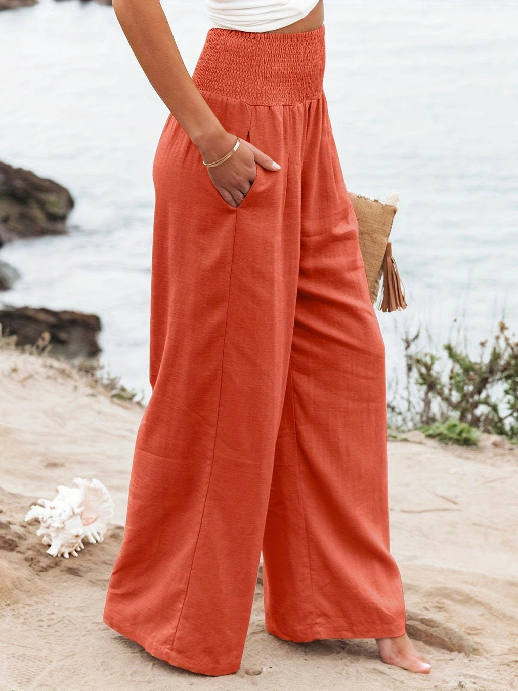Side view of women's coral high-waisted wide-leg linen pants with a flowy silhouette and soft drape.