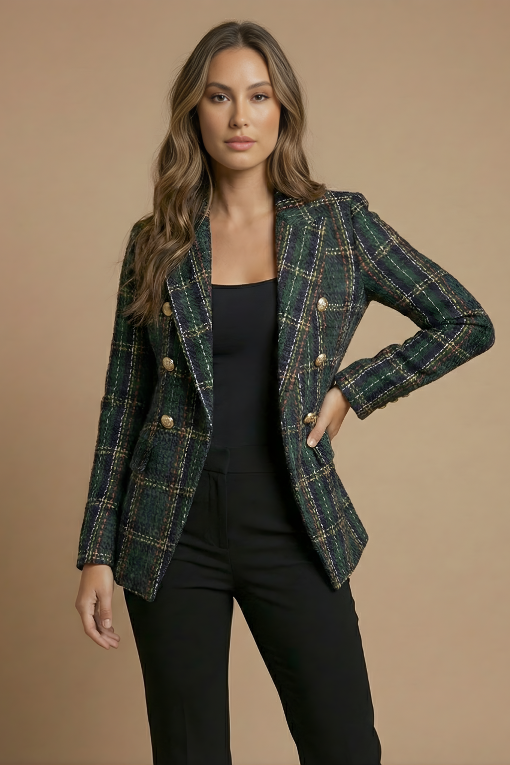 Woman wearing a dark green plaid tweed blazer with gold-tone buttons, notched lapels, flap pockets, and tailored fit over a black top and trousers.