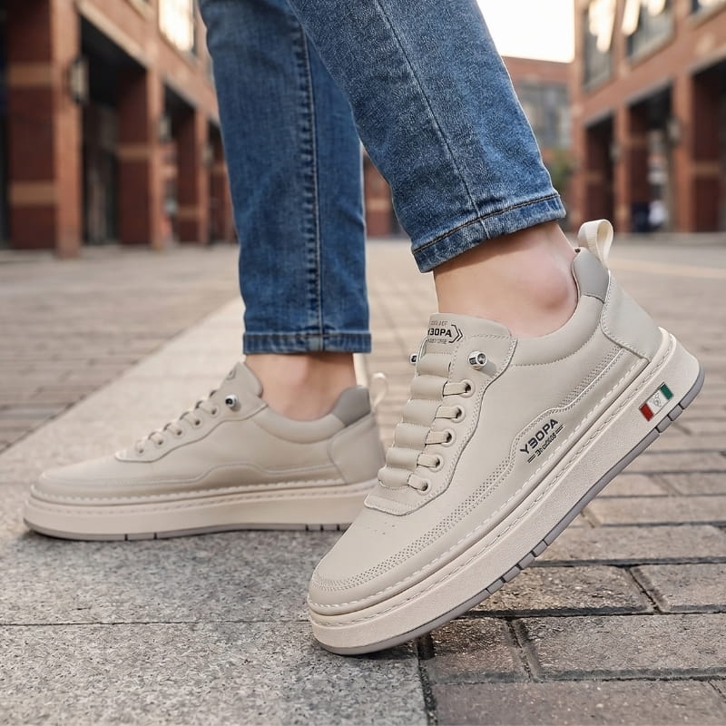 Person wearing beige leather chunky sneakers with jeans, walking on a cobblestone street