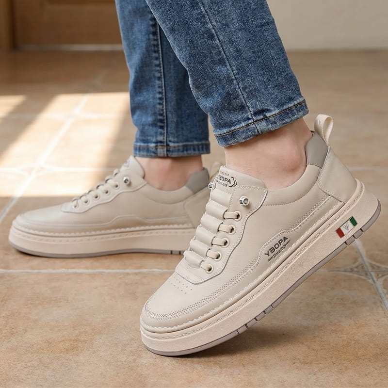 Person wearing beige leather chunky sneakers with jeans, standing on a sunlit terracotta tile floor