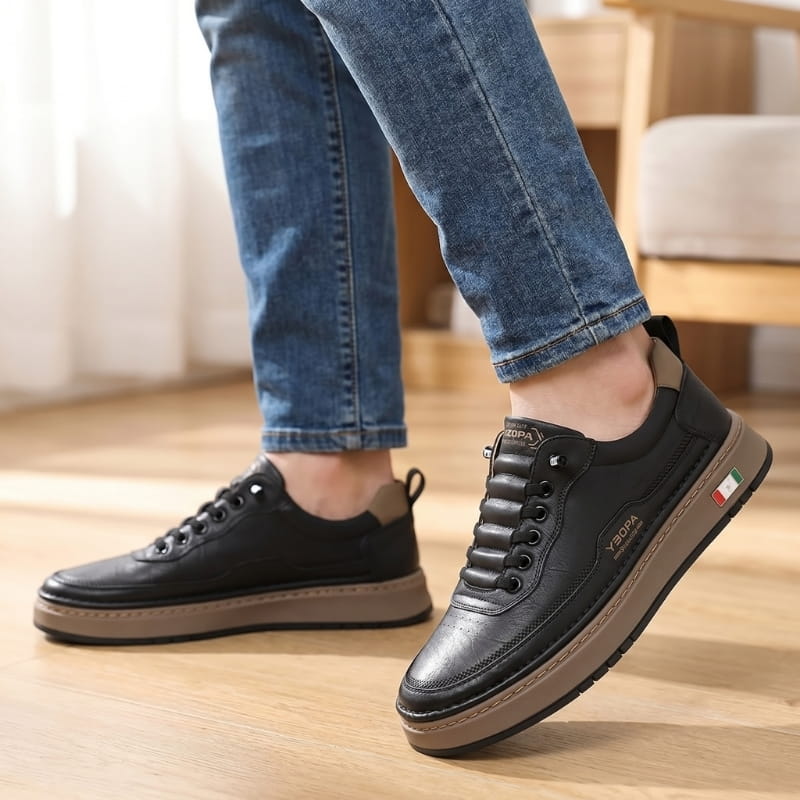 Person wearing black leather chunky sneakers with jeans, walking on a wood floor indoors