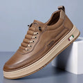 Brown leather chunky sneaker with tan sole and side patch detail propped diagonally against a white block on a blue studio background