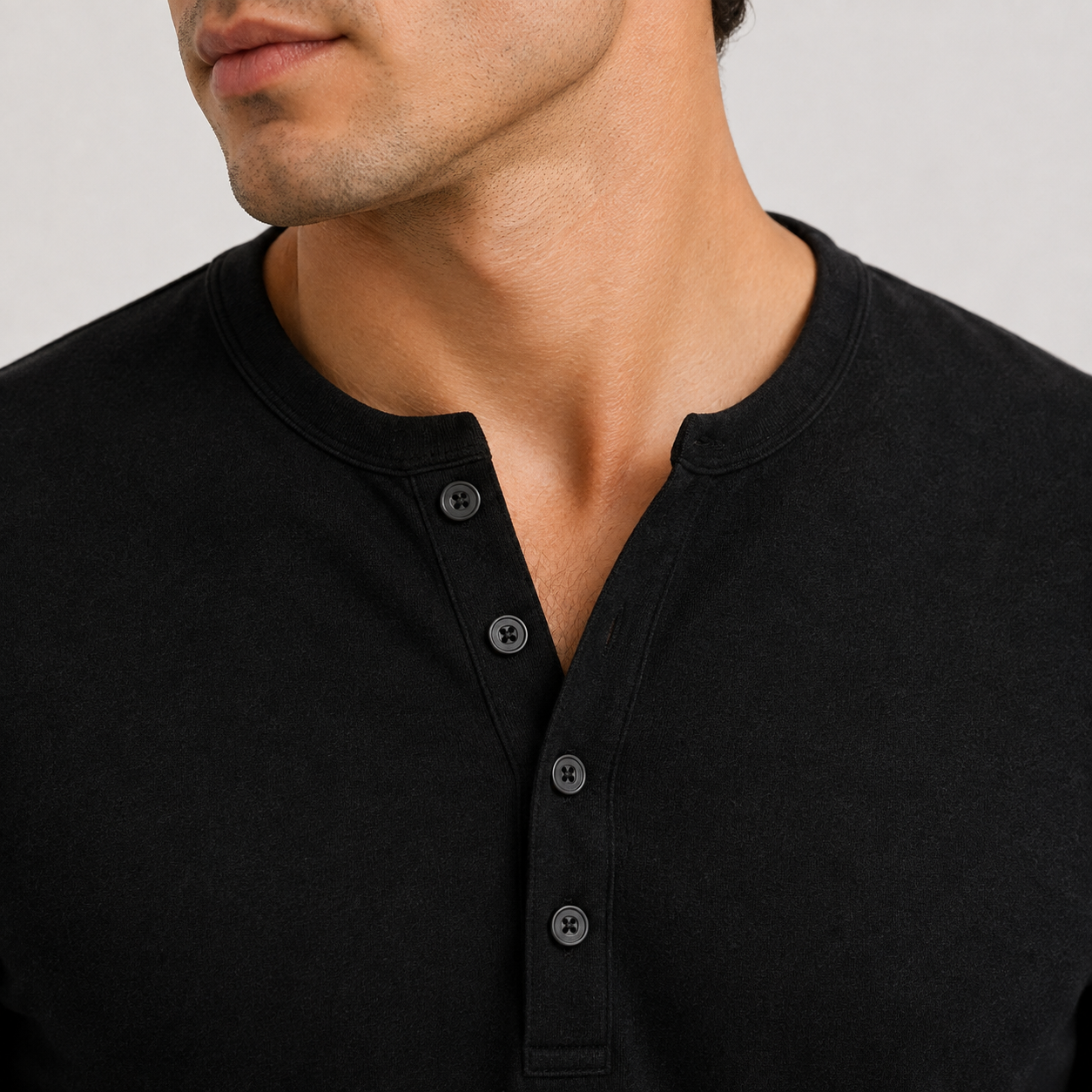 Close-up of the black Henley sweater showcasing the three-button placket, round neckline, and textured knit fabric.