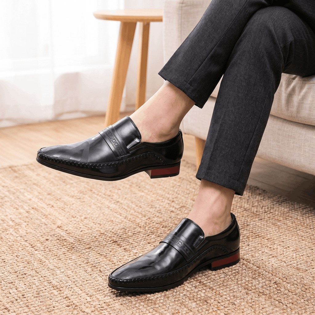 Crossed legs in dark gray trousers wearing black patent leather Leonardo loafers with burgundy heel accents over a jute rug