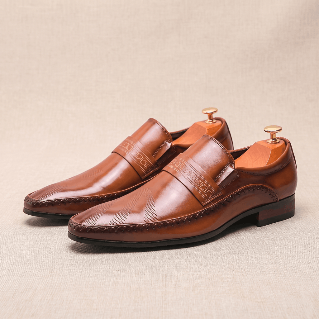 Pair of brown leather Leonardo loafers with etched band detail and shoe trees on beige backdrop