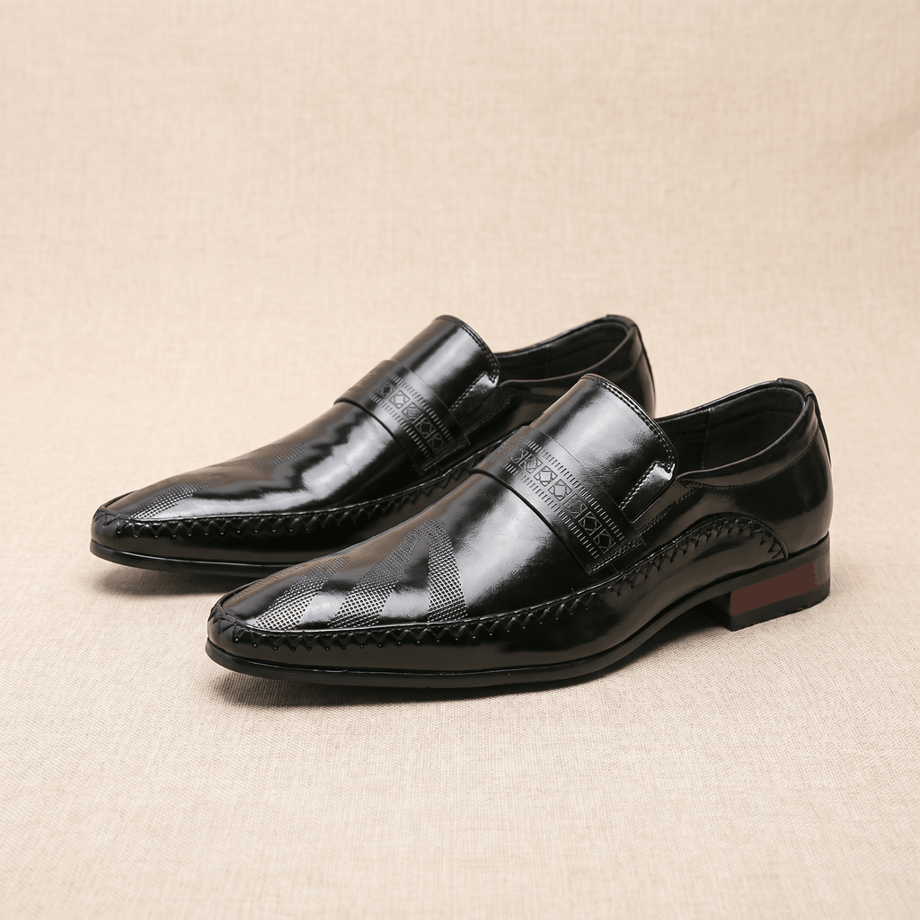 Pair of black patent leather Leonardo loafers with etched band and burgundy heel accent on beige backdrop