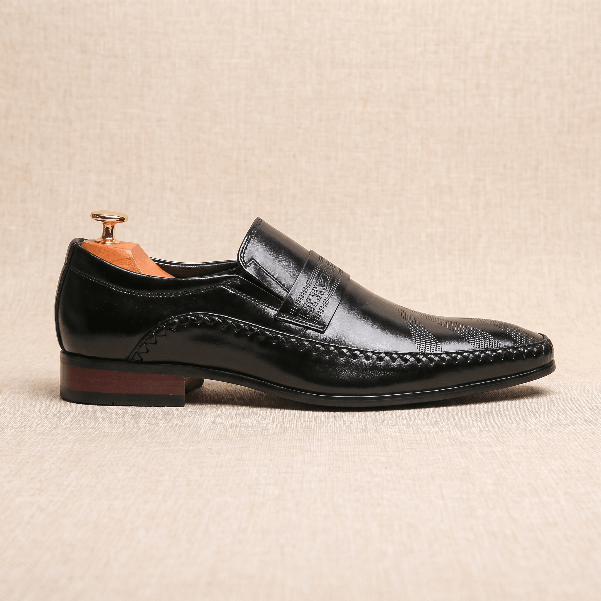 Single black patent leather Leonardo loafer shown in side profile with wooden shoe tree on beige backdrop