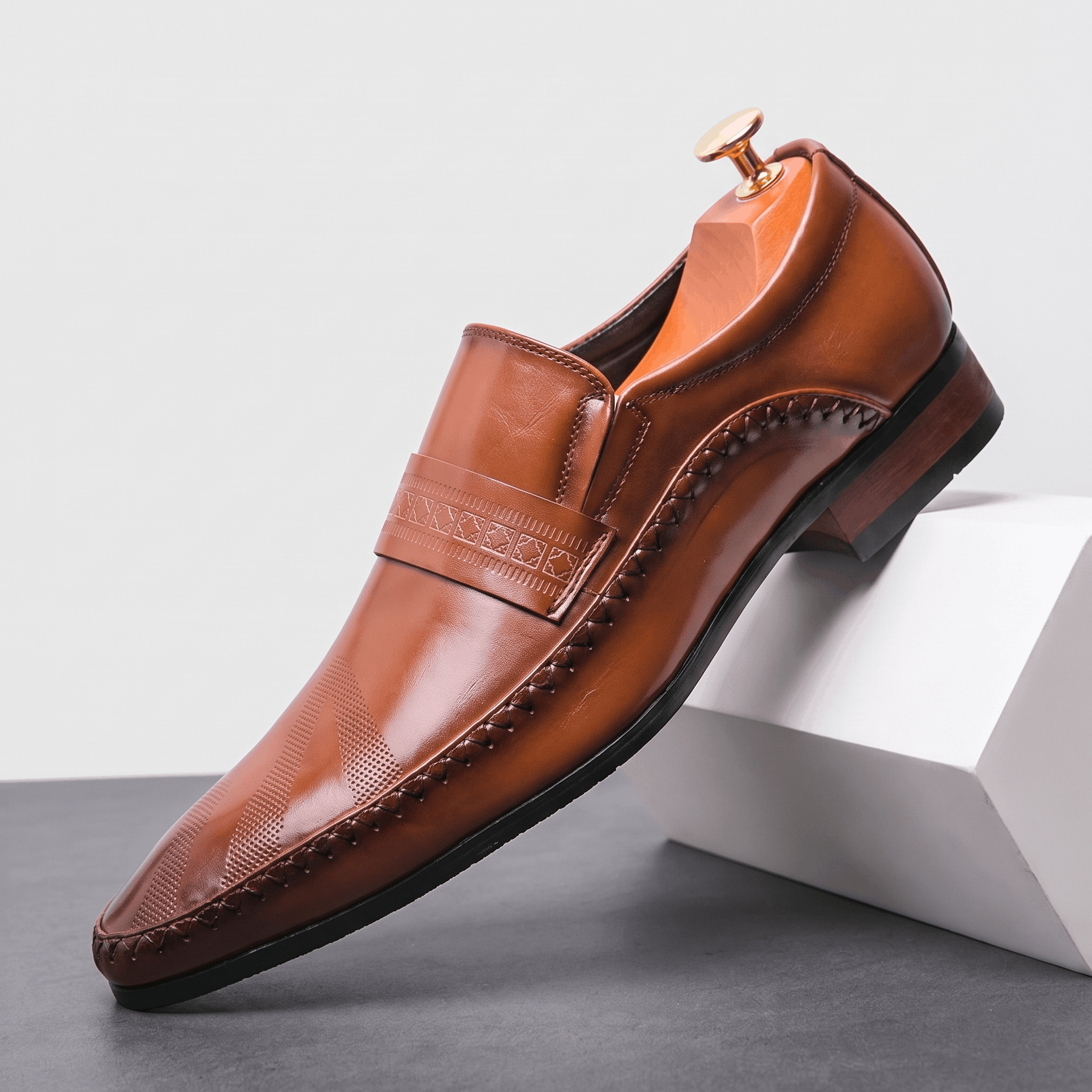 Single brown leather Leonardo loafer with etched band detail, propped against a white block in studio setting