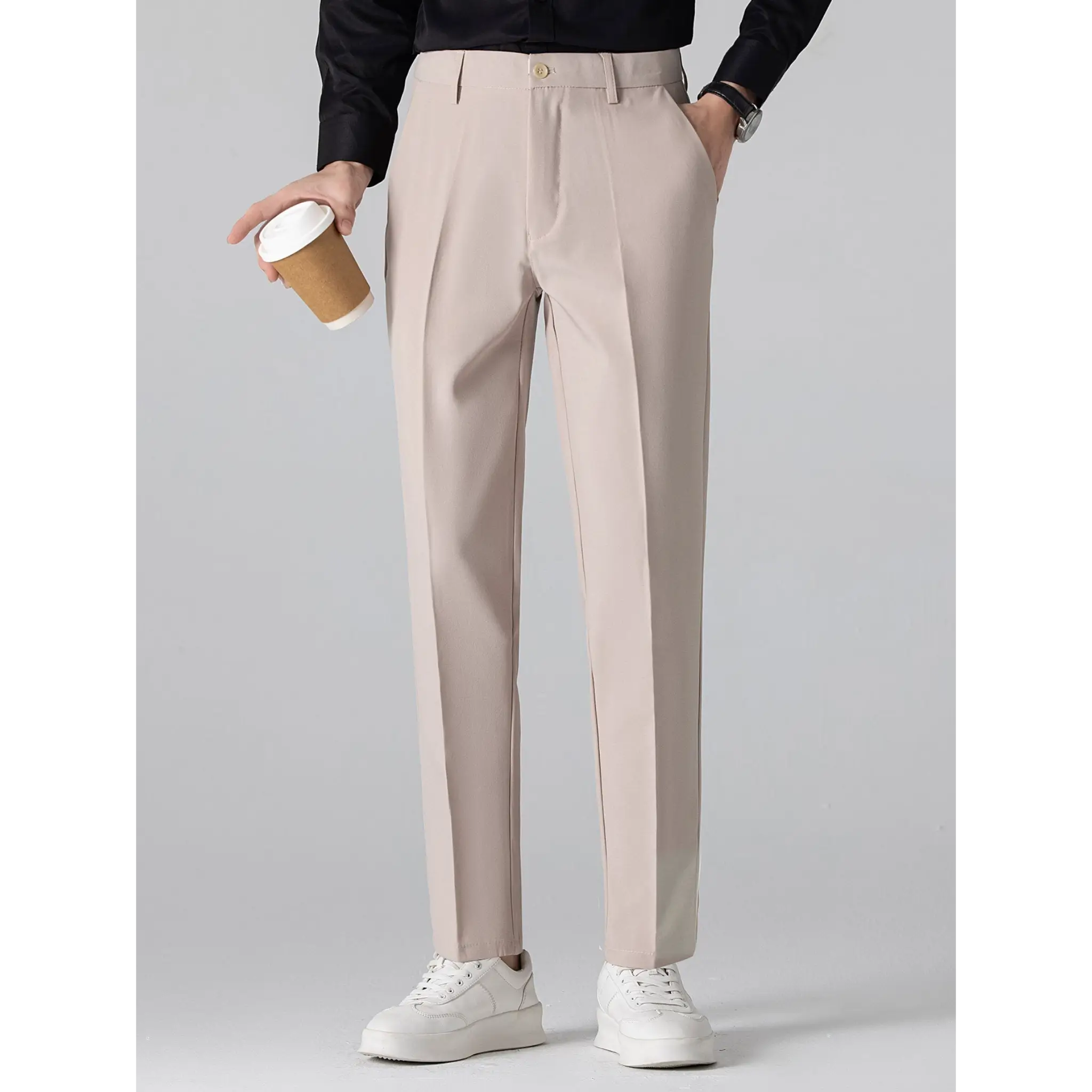 Man wearing beige tailored trousers paired with a black top while holding a coffee cup.