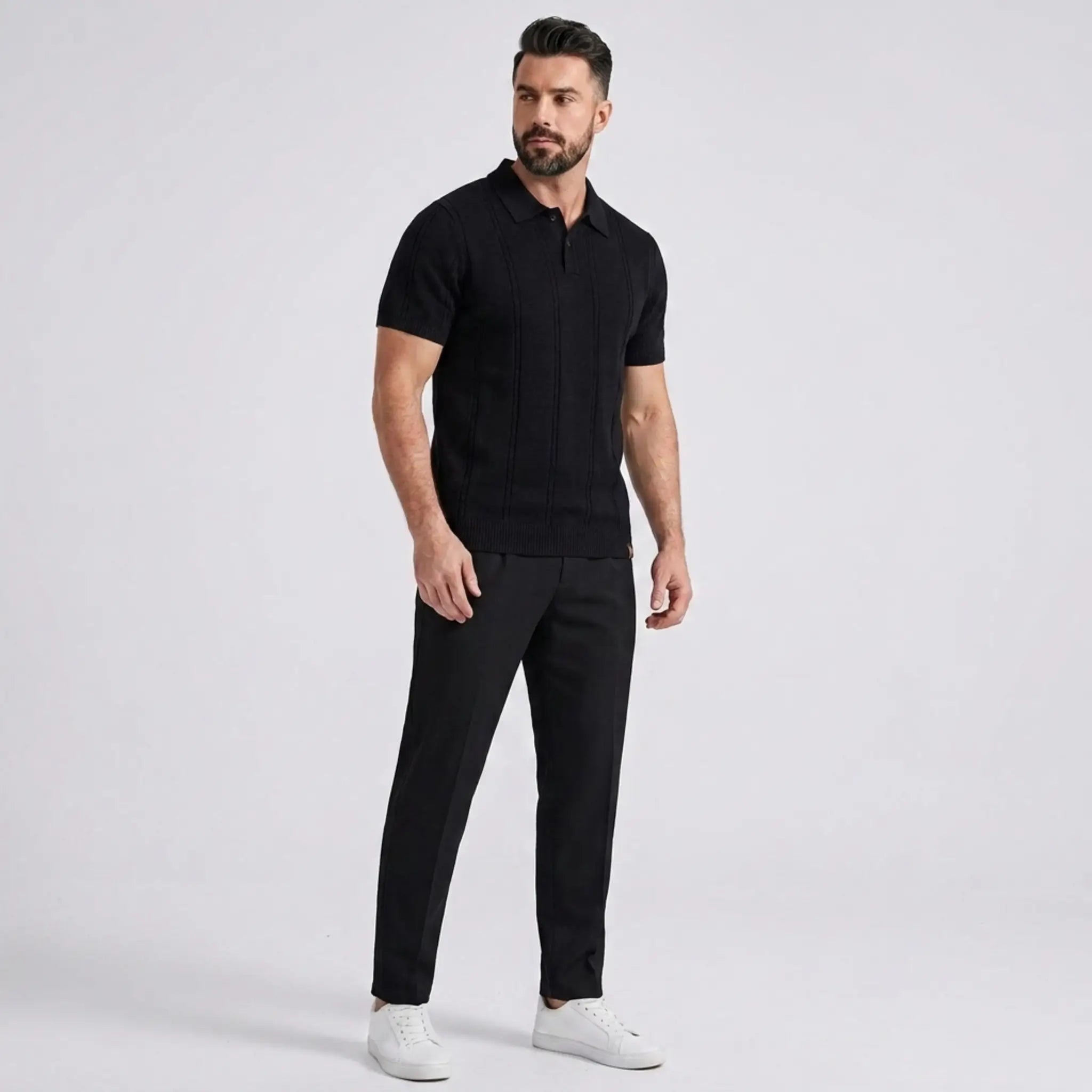 Man wearing a black short-sleeve knit polo shirt with black trousers in a full-body studio portrait.