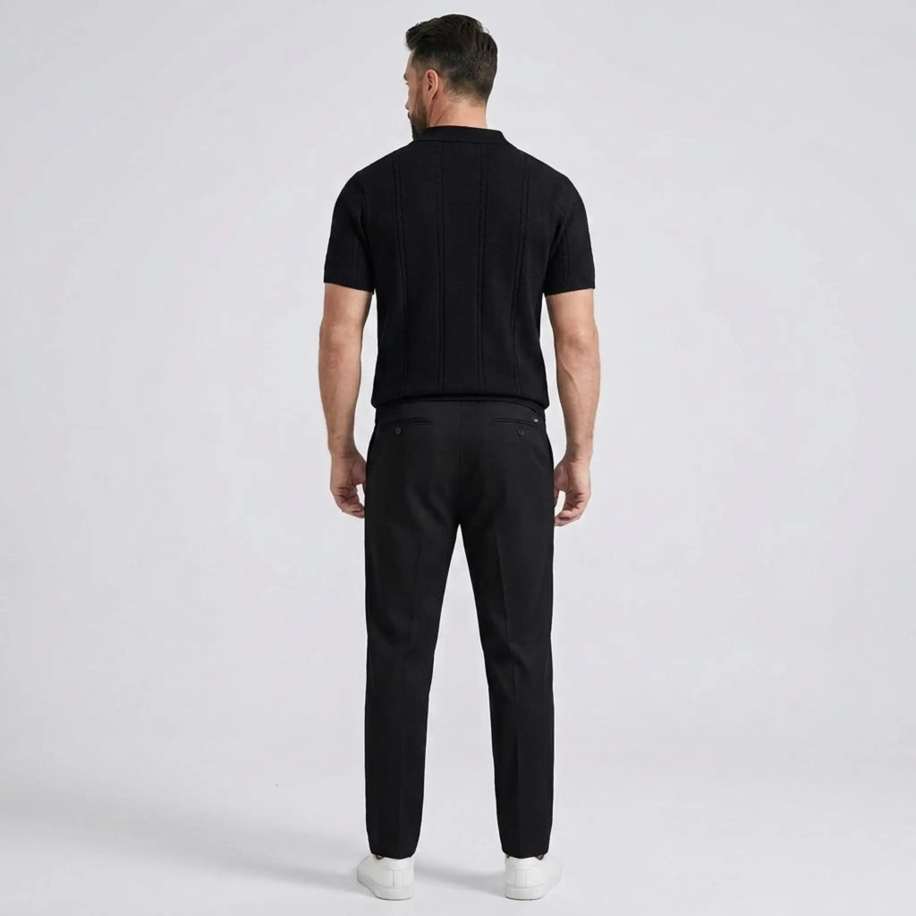 Back view of a man wearing a black short-sleeve knit polo shirt with black trousers.