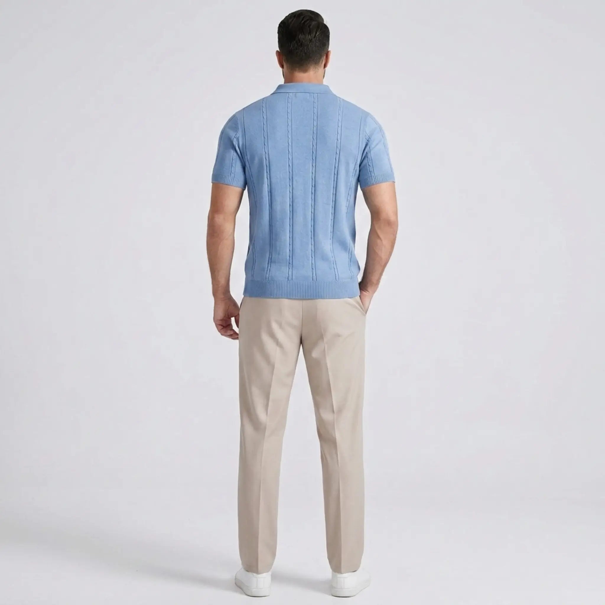 Back view of a man wearing a light blue short-sleeve knit polo shirt with beige trousers.