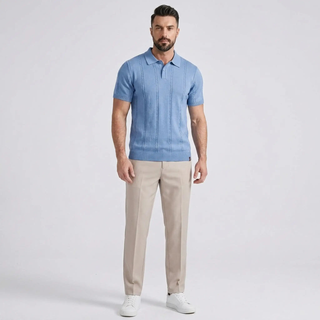 Man wearing a light blue short-sleeve knit polo shirt with beige straight-leg trousers and white sneakers in a full-body studio portrait.