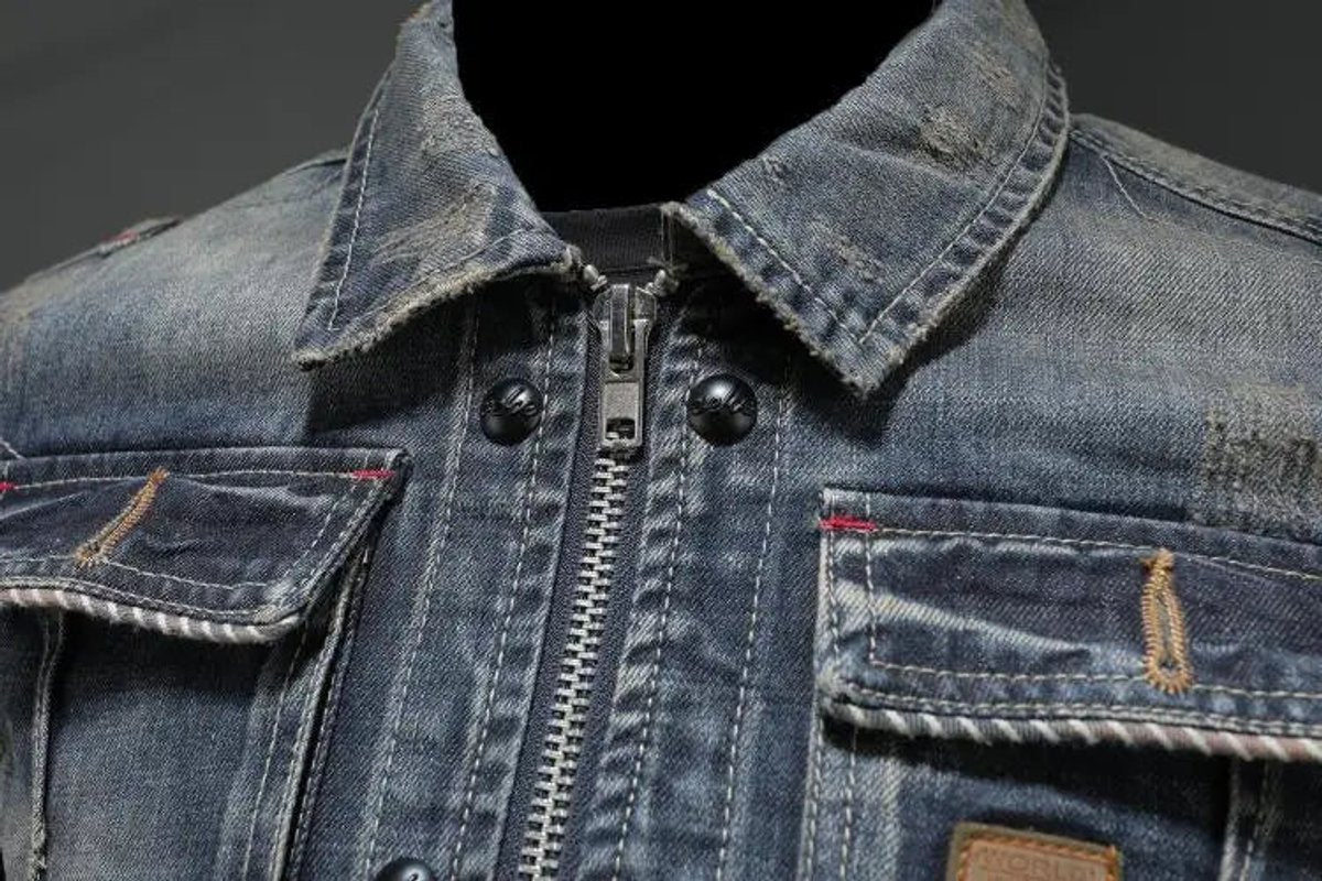 Close-up of the pointed collar, chest pocket, and faded denim texture on a men's vintage wash denim jacket.