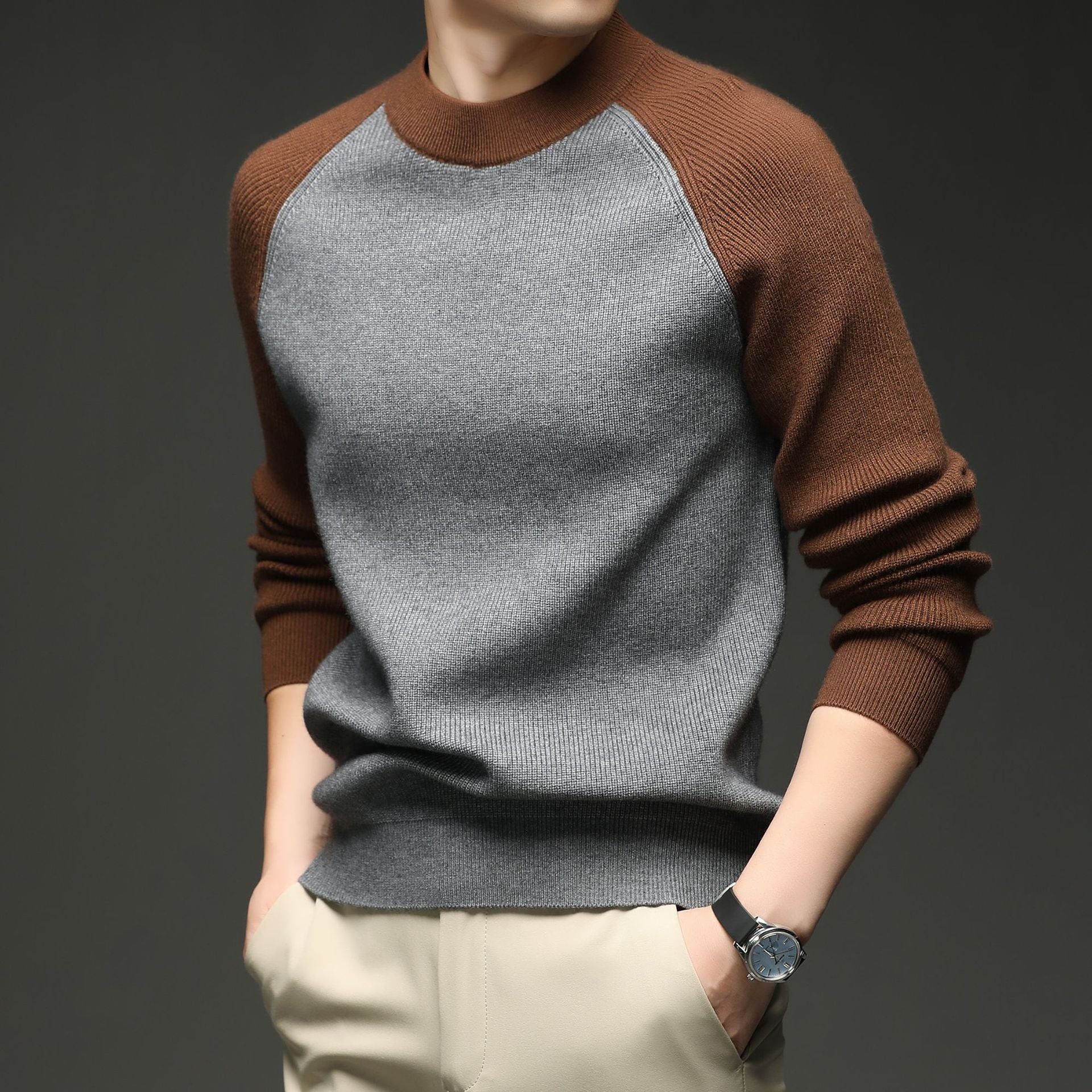 Man wearing grey and brown colorblock raglan knit sweater, close-up torso view with hand on hip