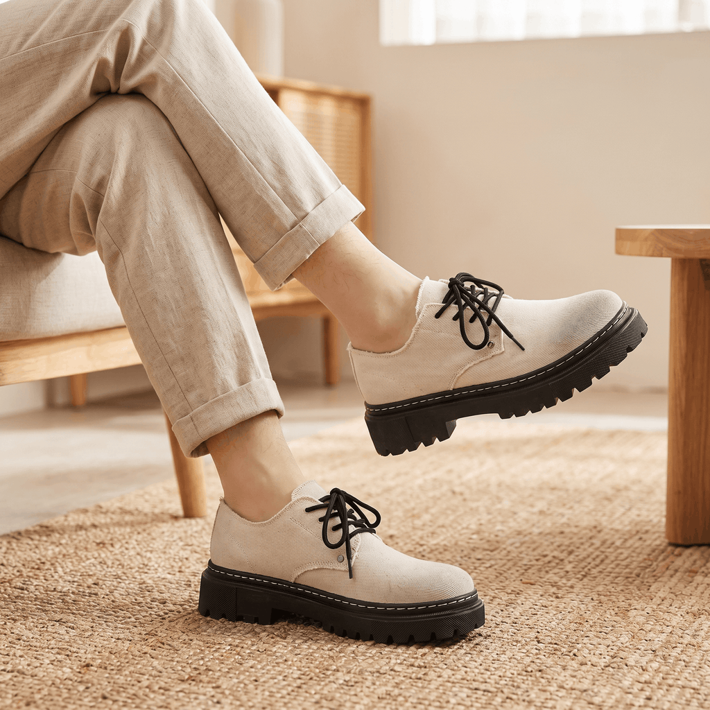Person seated with legs crossed wearing beige denim Manuel shoes over a jute rug indoors