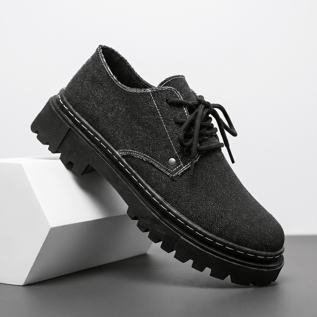 Single black denim Manuel lace-up shoe with white contrast stitching, propped against a white block in studio setting