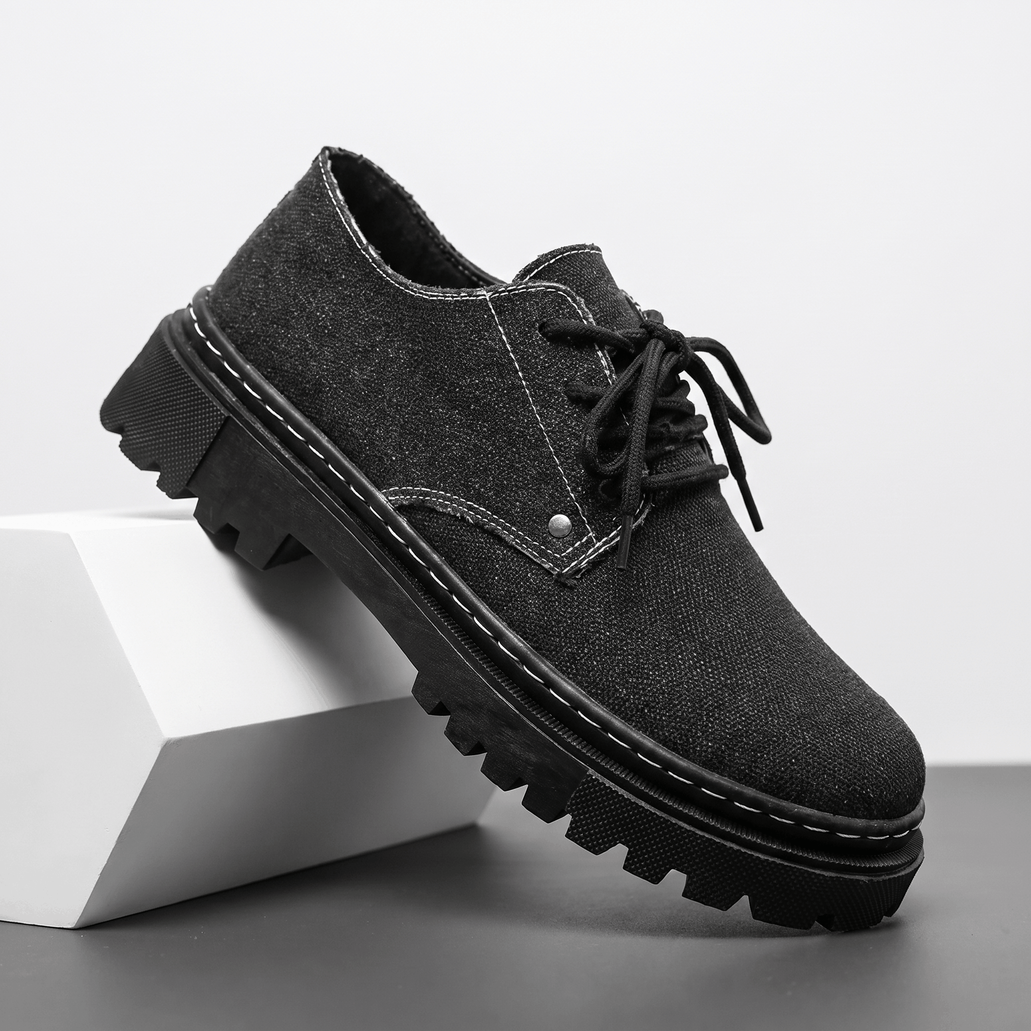 Single black denim Manuel lace-up shoe with white contrast stitching, propped against a white block in studio setting