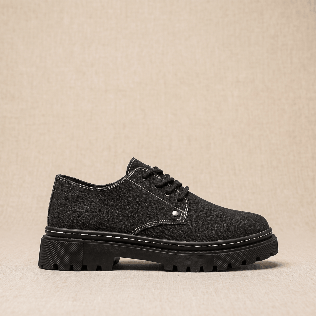 Single black denim Manuel lace-up shoe shown in side profile with white contrast stitching on beige backdrop