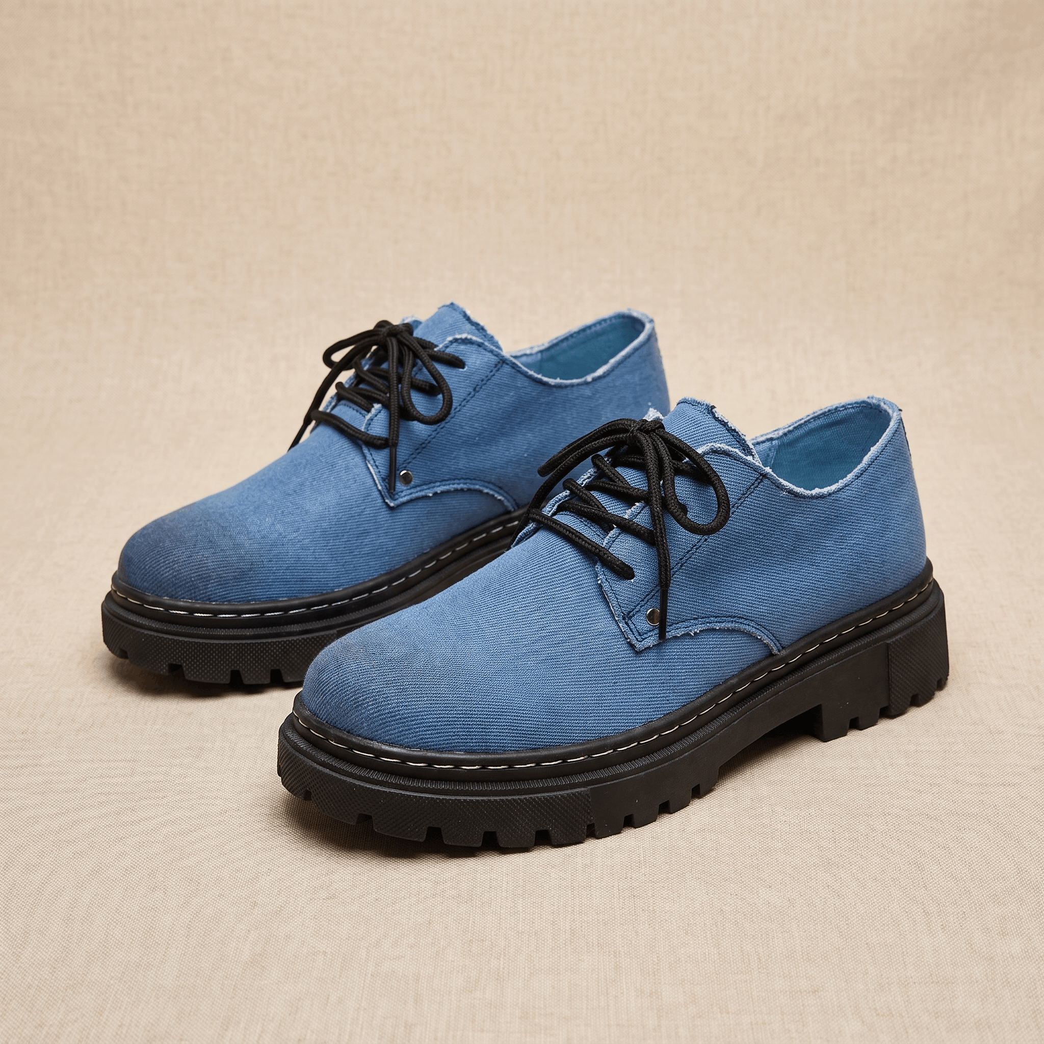 Pair of blue denim Manuel lace-up shoes with black rubber lug soles on beige backdrop