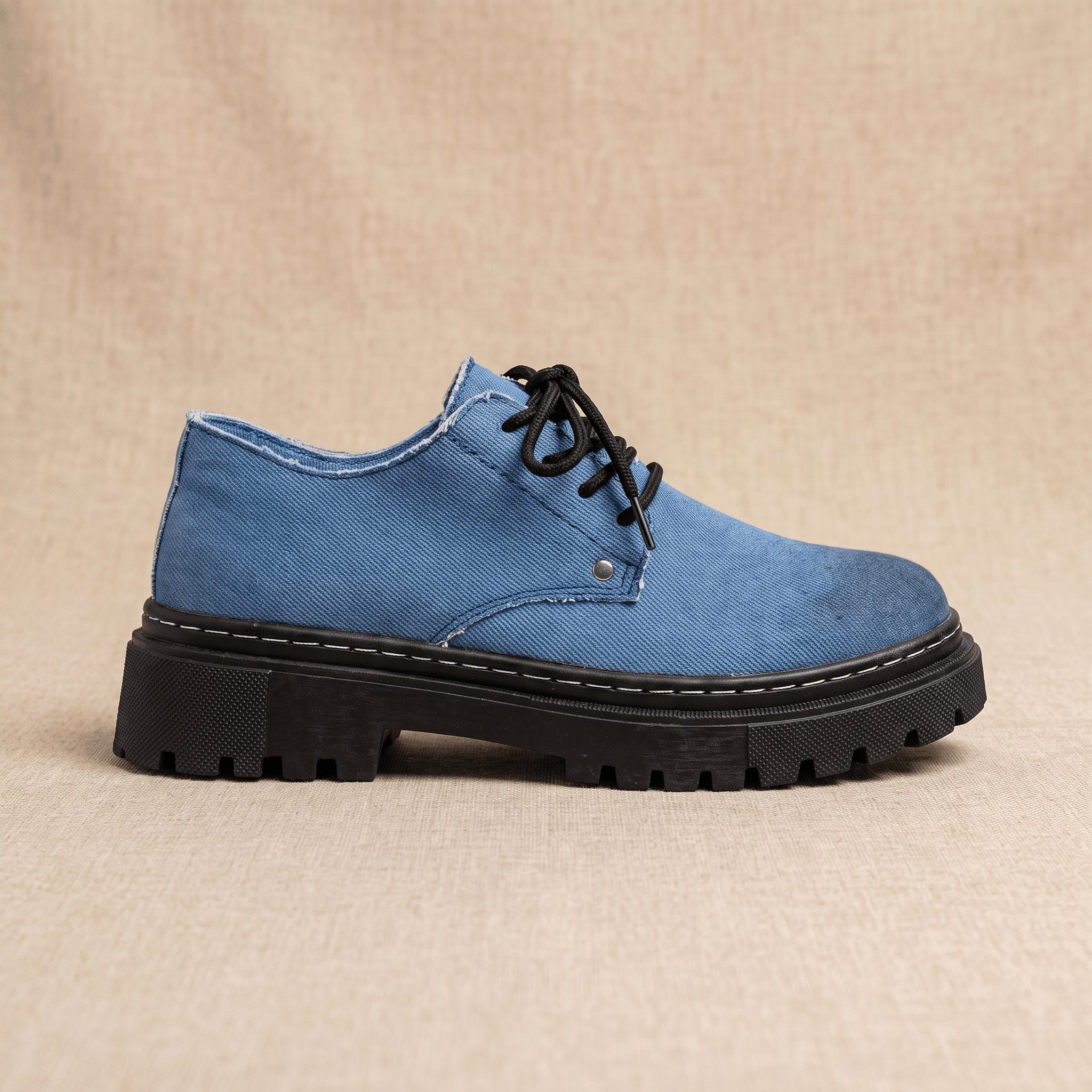 Single blue denim Manuel lace-up shoe shown in side profile with black lug sole on beige backdrop