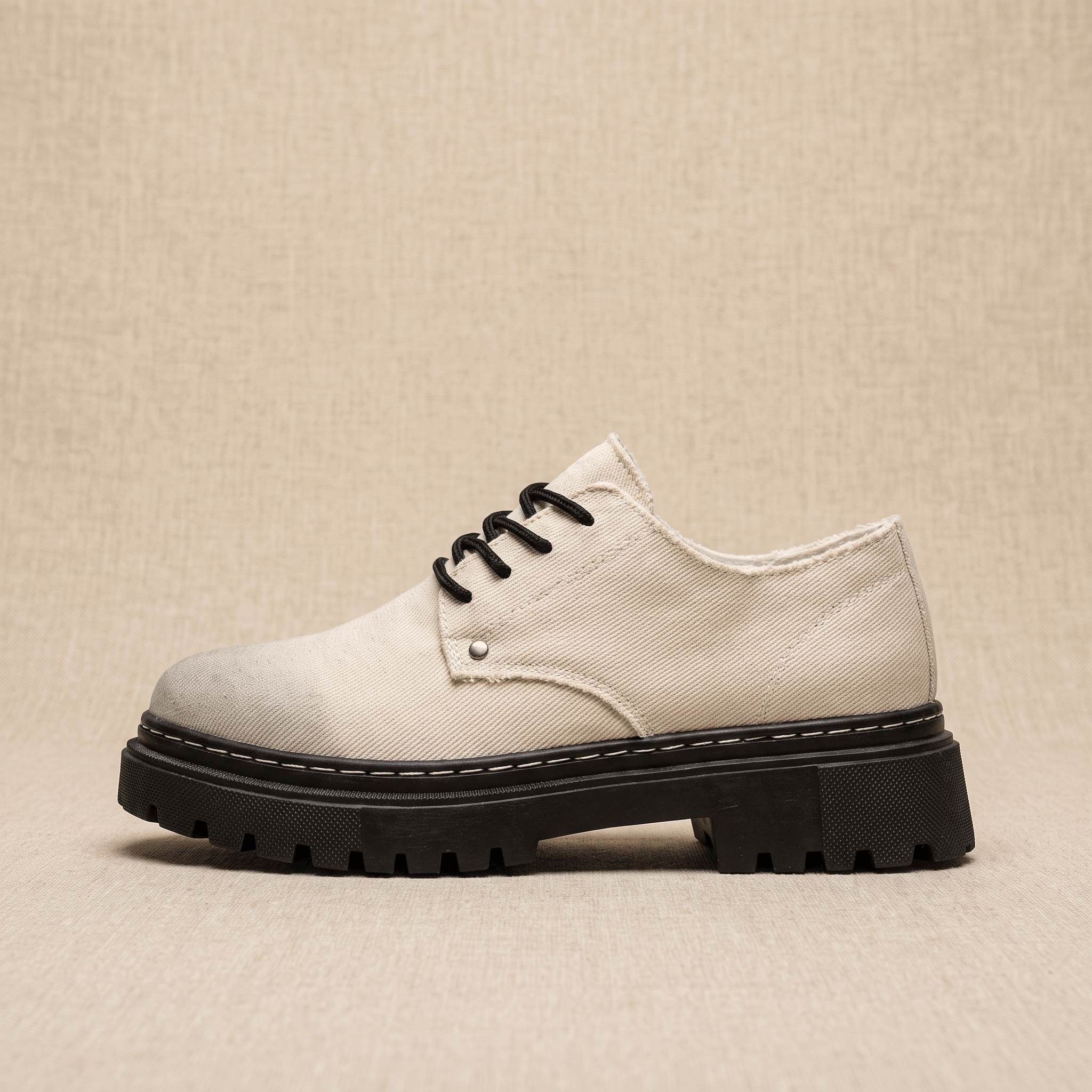 Single beige denim Manuel lace-up shoe shown in side profile with black lug sole on tan backdrop