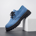 Single blue denim Manuel lace-up shoe with black rubber lug sole, propped against a white block in studio setting
