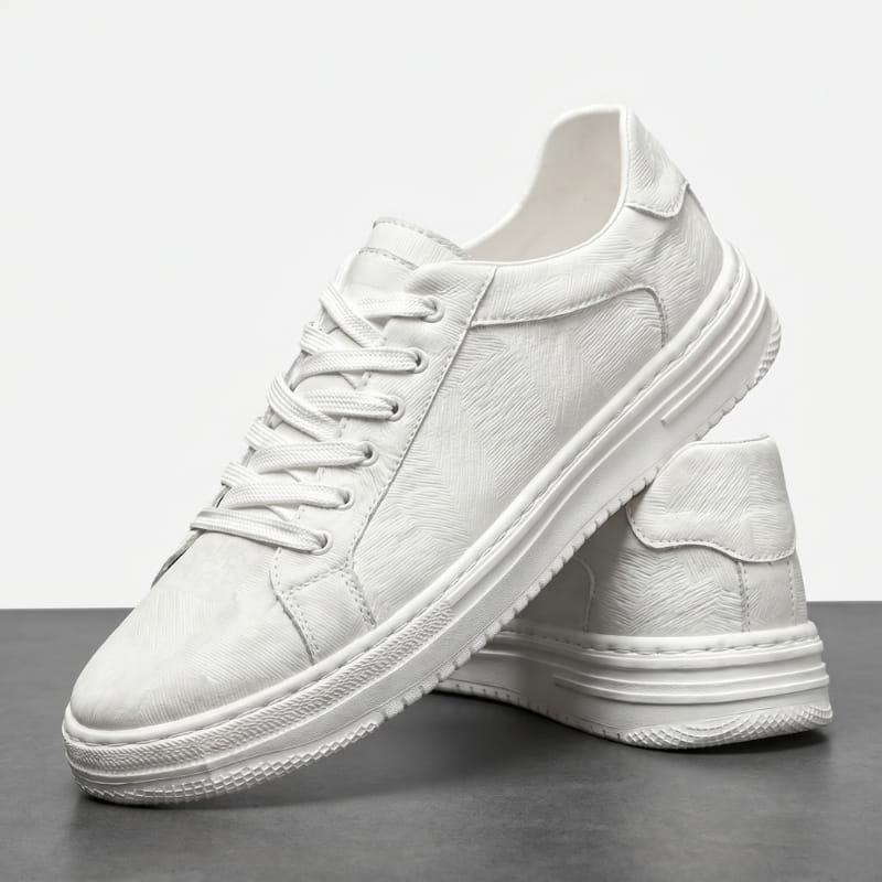 Pair of white leather sneakers with textured finish, one shoe leaning against the other on a dark surface