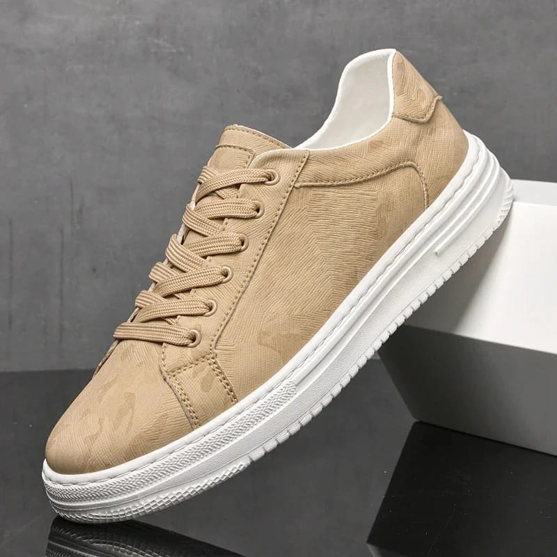 Beige leather sneaker with subtle camo texture and white sole propped diagonally against a white block on a gray background