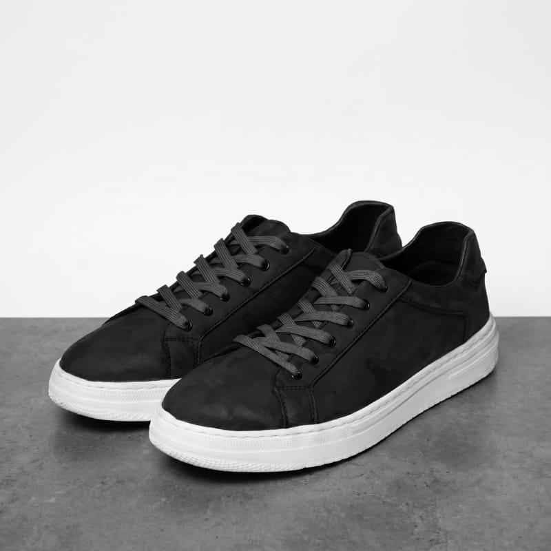 Pair of black leather sneakers with white soles facing forward on a concrete surface against a white background