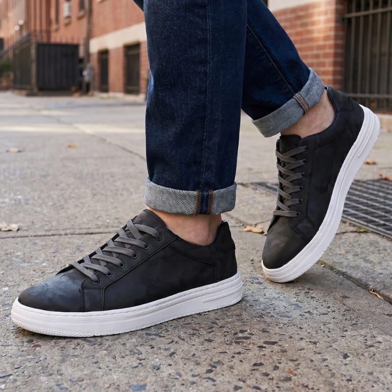 Person wearing black leather sneakers with cuffed jeans, walking on an urban street
