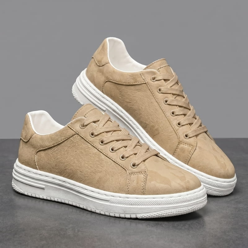 Pair of beige leather sneakers with white soles stacked at an angle on a gray studio background