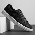 Black leather sneaker with subtle camo texture and white sole propped diagonally against a white block, monochrome studio shot