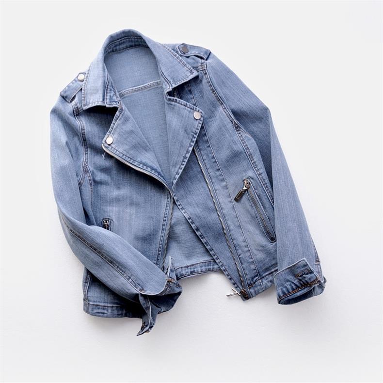Folded light wash women's denim moto jacket showcasing the asymmetrical zip front, lapel collar, and distressed denim finish.