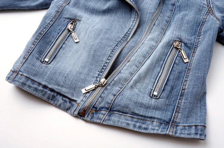 Close-up of the zippered front pockets and hem detailing on a light wash women's denim moto jacket.