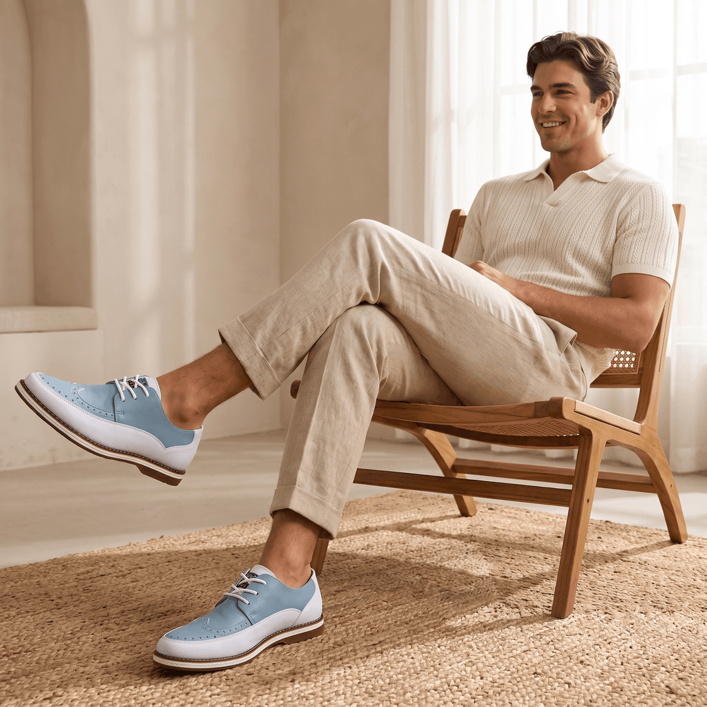 Smiling man in cream polo shirt seated with legs extended, wearing white and blue two-tone Mauro brogues, in a bright airy room on a jute rug
