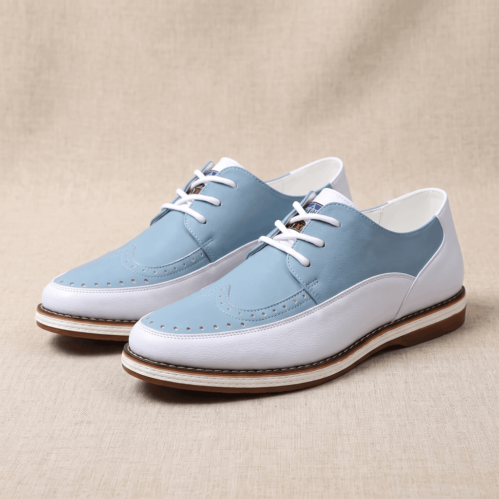 Pair of white and blue two-tone leather Mauro brogues with perforated wingtip detailing, resting on a beige fabric backdrop