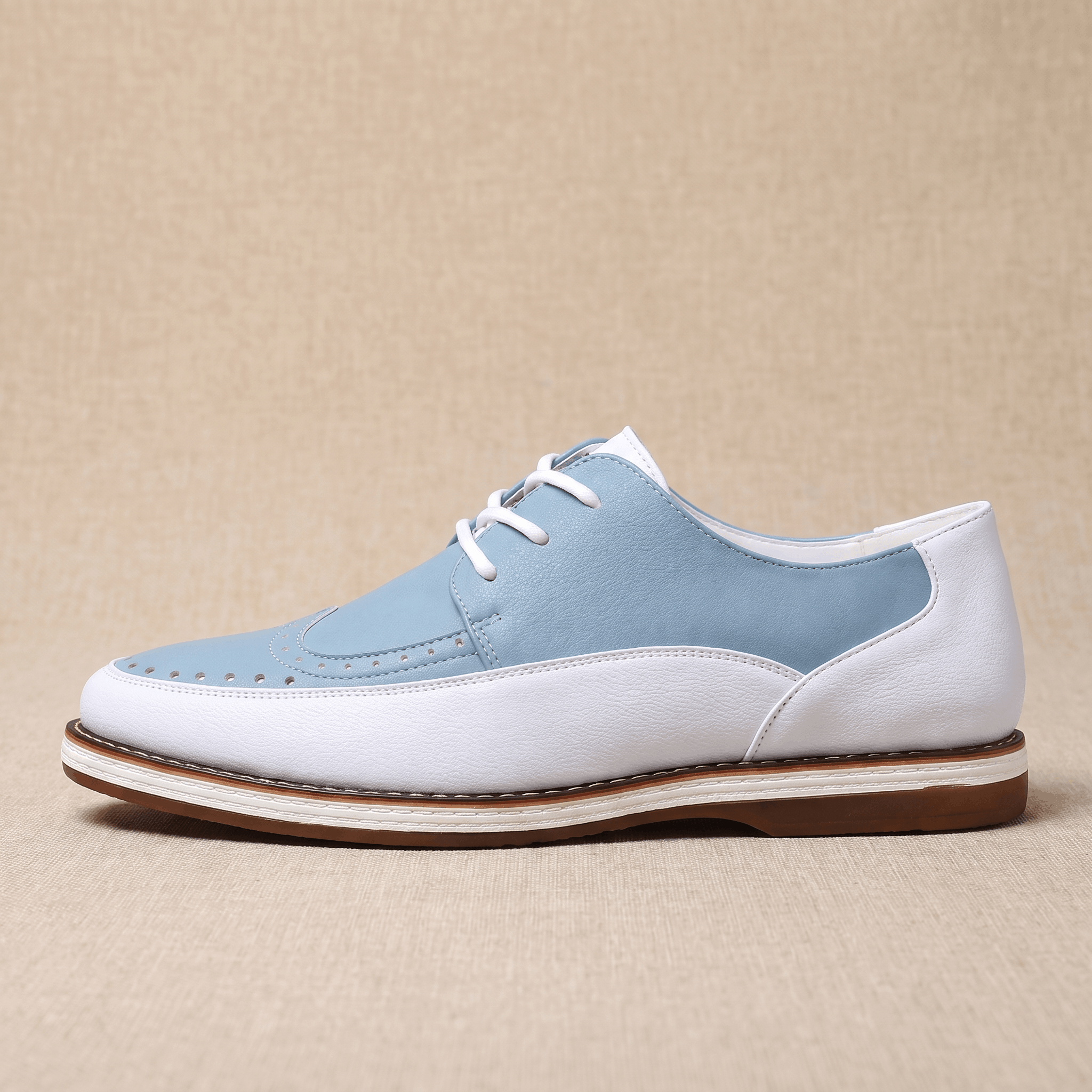 Side profile of a single white and blue two-tone leather Mauro brogue with moc-toe stitching, resting on a beige surface