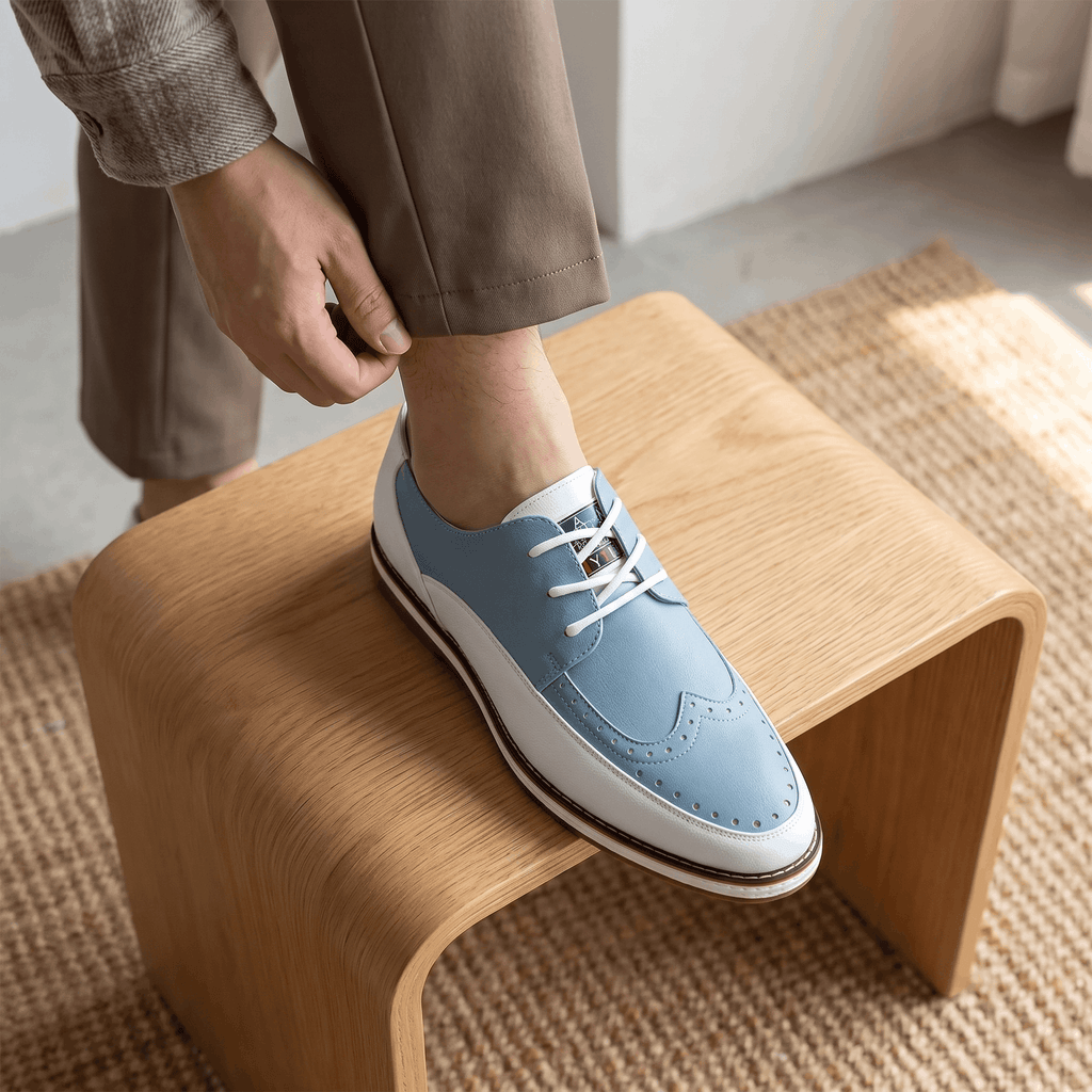 Man adjusting trouser cuff with foot resting on a wooden bench, wearing white and blue two-tone Mauro brogue over a jute rug