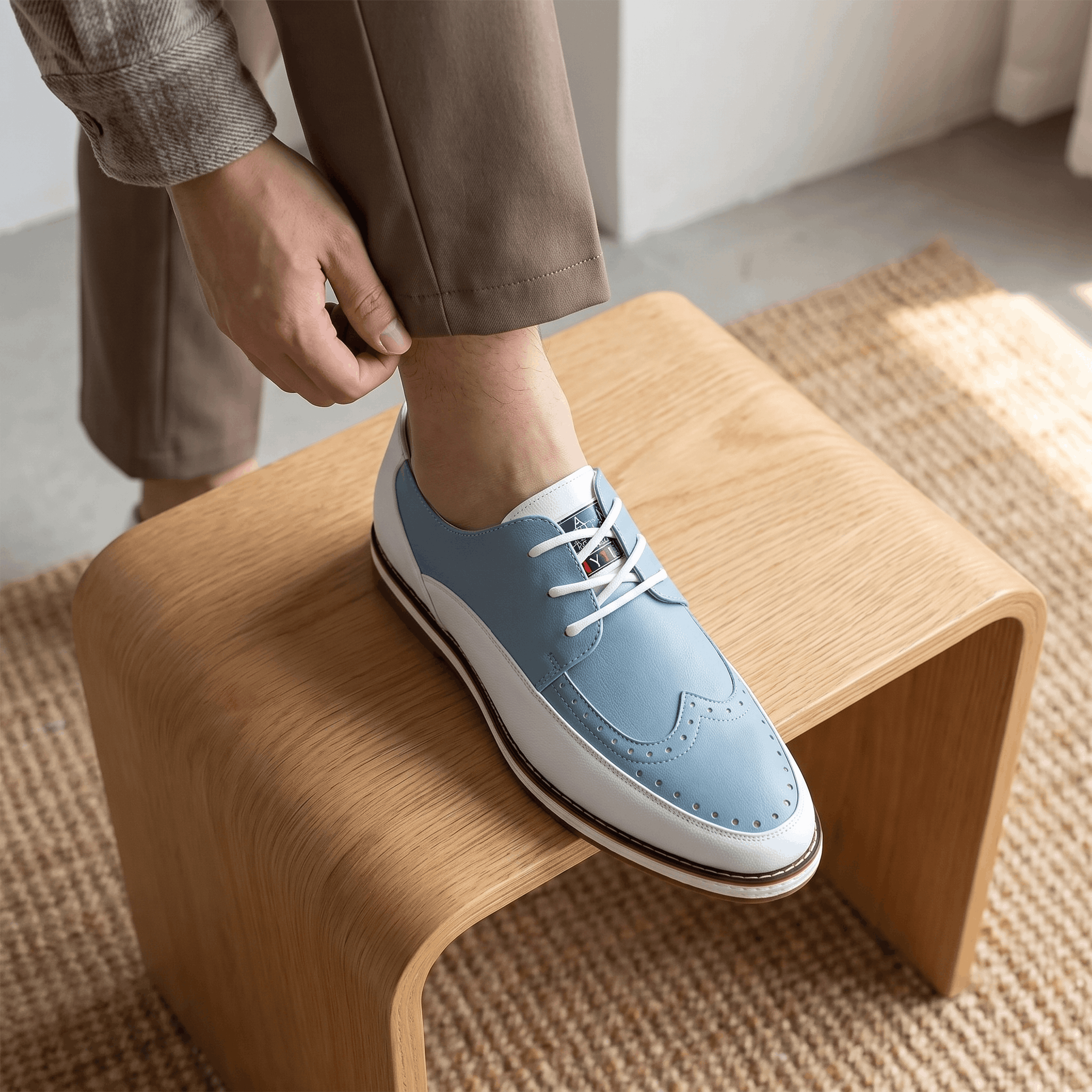 Man adjusting trouser cuff with foot resting on a wooden bench, wearing white and blue two-tone Mauro brogue over a jute rug