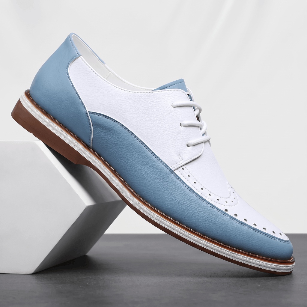 Single white and blue two-tone leather Mauro brogue propped against a white pyramid block, showing perforated toe cap and heel