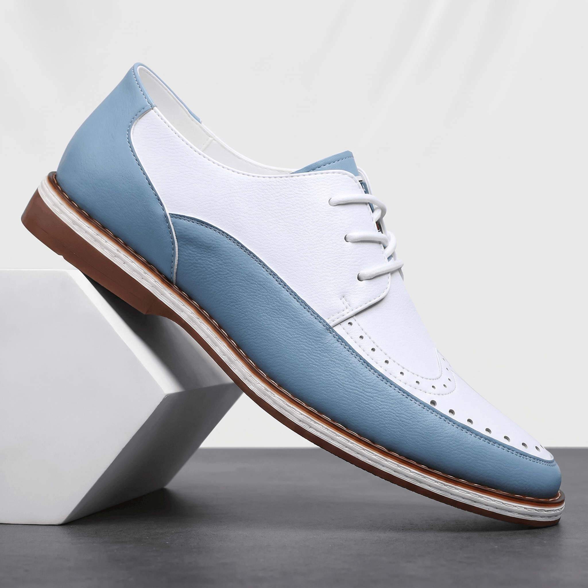 Single white and blue two-tone leather Mauro brogue propped against a white pyramid block, showing perforated toe cap and heel