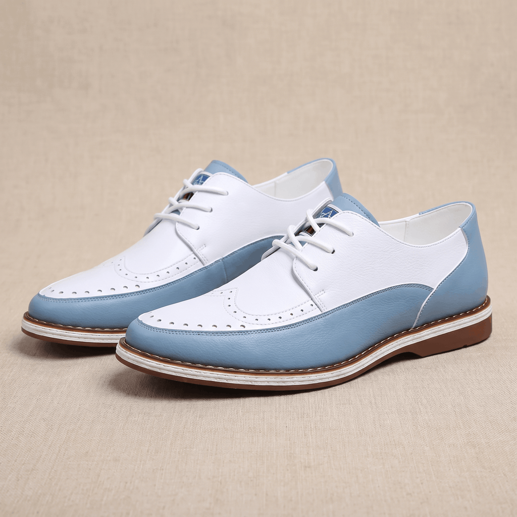 Pair of white and blue two-tone leather Mauro brogues angled together on a beige surface, showing perforated detailing along the toe